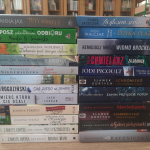 W bibliotece. Na stoliku ustawione poziomo książki, grzbietem do przodu.