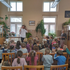 W bibliotece. Grupa dzieci na spotkaniu autorskim. Patrzą na prowadzącego spotkanie.