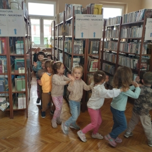 W bibliotece. Grupa dzieci bawi się w pociąg zwiedzający bibliotekę.