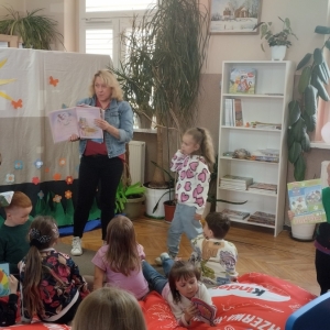 W bibliotece. Grupa dzieci spędza czas w bibliotece. Kobieta pokazuje książki, które są dostępne w bibliotece. 