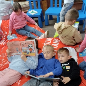 Dzieci spędzają czas w bibliotece. Siedzą na pufach i przeglądają książki.