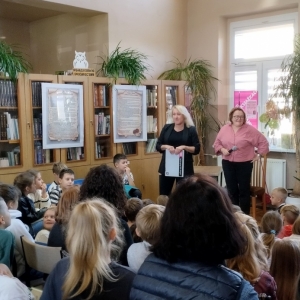 W bibliotece. Grupa osób patrzy na dwie kobiety, które prowadzą spotkanie.