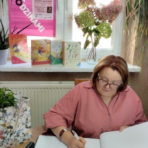 W bibliotece. Spotkanie autorskie. Pisarka wpisuje się do księgi pamiątkowej biblioteki.