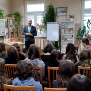W bibliotece. Grupa osób patrzy na mężczyznę, który prowadzi spotkanie.