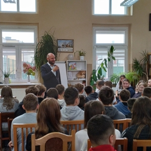 W bibliotece. Grupa osób patrzy na mężczyznę, który prowadzi spotkanie.