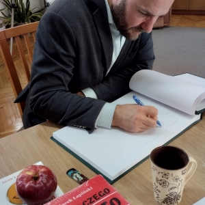 W bibliotece. Spotkanie autorskie. Pisarz wpisuje się do księgi pamiątkowej biblioteki.