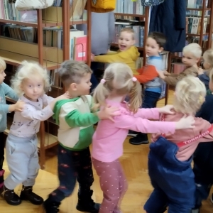 W bibliotece. Grupa dzieci bawi się w pociąg zwiedzający bibliotekę.