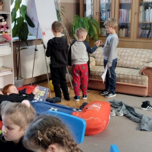 W bibliotece. Grupa dzieci gra w kalambury, druga grupa wykonuje prace plastyczne.