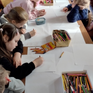 W bibliotece. Przy stolikach siedzą dzieci i malują na bloku rysunkowym.