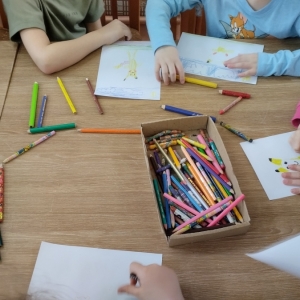 W bibliotece. Dzieci siedzą przy stolikach i wykonują prace plastyczne.