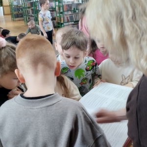W bibliotece. Grupa dzieci z zainteresowaniem przegląda książkę.