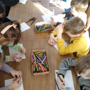 W bibliotece. Dzieci siedzą przy stolikach i wykonują prace plastyczne.