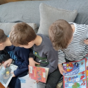 W bibliotece. Czterej chłopcy siedzą na kanapie i przeglądają książki.