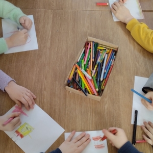 W bibliotece. Dzieci siedzą przy stolikach i wykonują prace plastyczne.