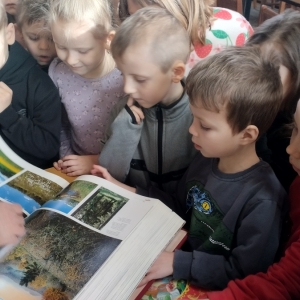 W bibliotece. Grupa dzieci z zainteresowaniem przegląda książkę.