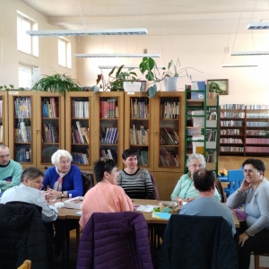 W bibliotece. Grupa osób siedzi przy stolikach.