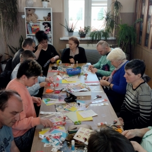 W bibliotece. Podczas warsztatów. Grupa osób siedzi przy stolikach i wykonuje zakładki do książek.