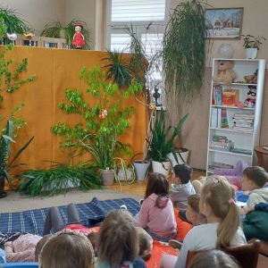 W bibliotece. Scena przygotowana do teatrzyku. Dekoracja to zielone rośliny na miodowym tle. 