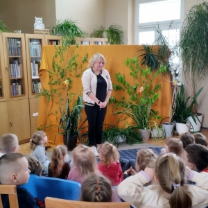 W bibliotece. Dekoracja sceny. Dzieci patrzą w stronę prowadzącej spotkanie kobiety.
