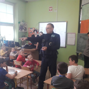 Klasa szkolna. Finał konkursu plastycznego. Dzieci słuchają pogadanki prowadzonej przez policjanta.