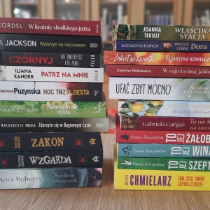 W bibliotece. Na stoliku ustawione książki. W tle regały z książkami.