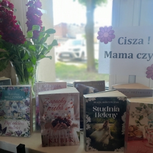 W bibliotece. Na parapecie stoją książki. Na oknie przyklejona papierowa kartka, na niej napis "Cisza! Mama czyta"