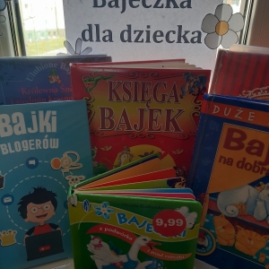 W bibliotece. Na parapecie stoją książki. Na oknie przyklejona papierowa kartka, na niej napis "Bajeczka dla dziecka"