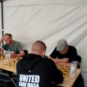 W plenerze. W trakcie trwania turnieju szachowego. Przy stolikach siedzą gracze.