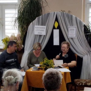 W bibliotece. Przy stoliku siedzą trzy osoby.