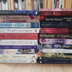 W bibliotece. Na stoliku ustawione książki. W tle regały z książkami.