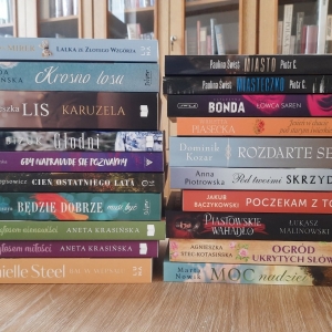 W bibliotece. Na stoliku ustawione książki. W tle regały książkami.
