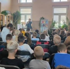 W bibliotece. Grupa osób patrzy na mężczyznę, który prowadzi spotkanie.