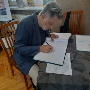 W bibliotece. Spotkanie autorskie. Pisarz wpisuje się do księgi pamiątkowej biblioteki.