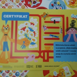 Na stoliku leżą plakaty, naklejki oraz certyfikat dla biblioteki za udział w projekcie.