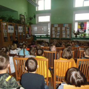 W pomieszczeniu biblioteki. Grupa dzieci ogląda film, który jest wyświetlany na ekranie projektora.