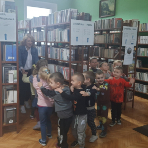 W pomieszczeniu biblioteki. Grupa dzieci uczestniczy w zajęciach ruchowych.