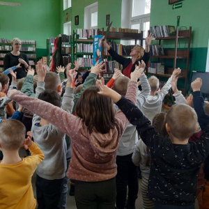 W pomieszczeniu biblioteki. Grupa dzieci uczestniczy w zajęciach ruchowych.