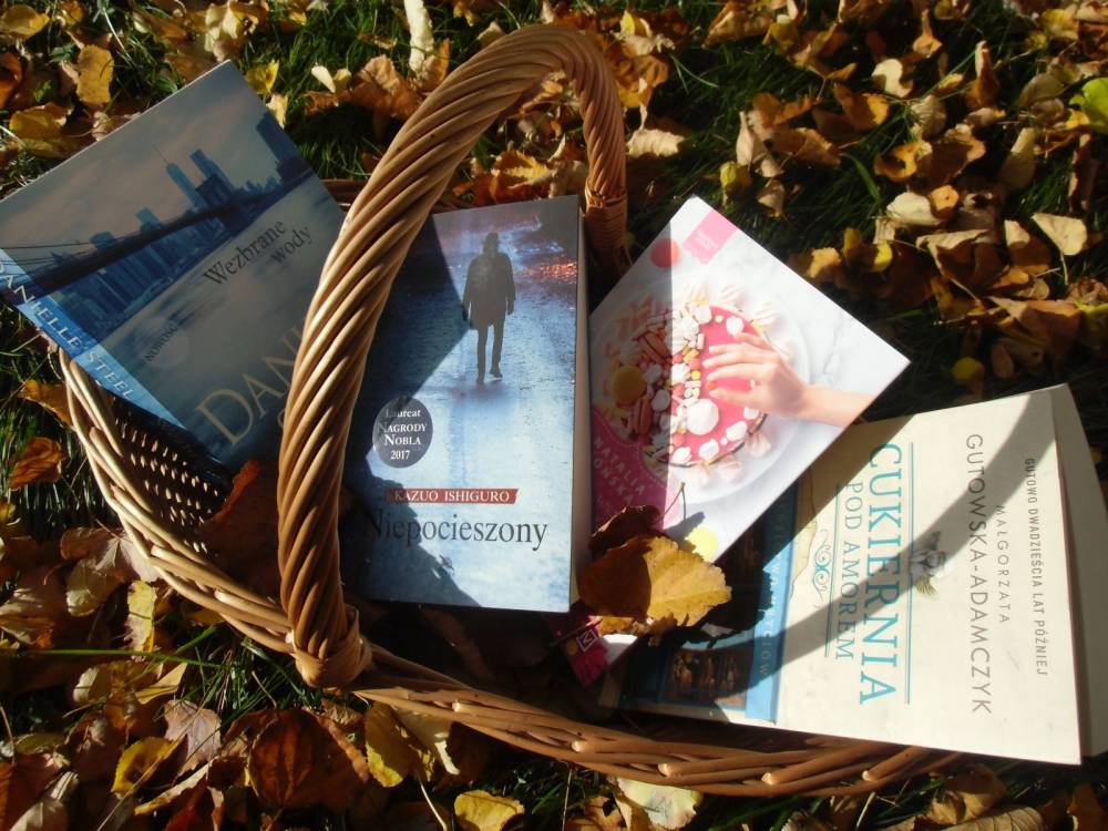 Cztery książki w wiklinowym koszyku. Koszyk stoi na trawniku. Wokół leżą pożółkłe liście